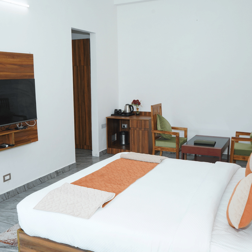 Spacious guest bedroom view showing a double bed, wall-mounted flat-screen television, tea setup, and wooden seating area - Five Elements Hotels, Corbett Crown Resort, Jim Corbett