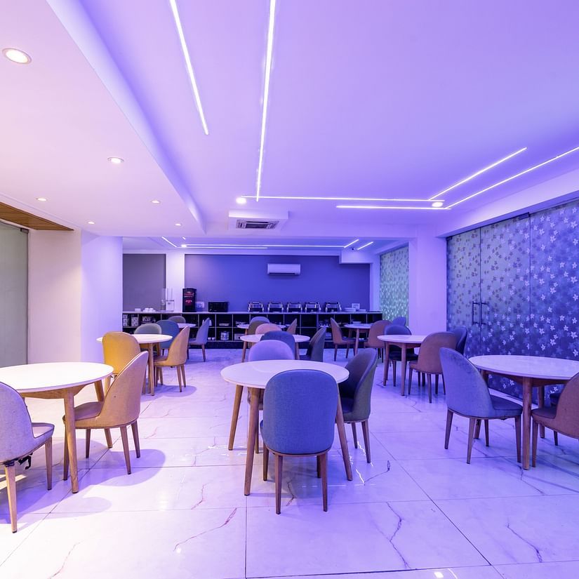 Chairs and tables placed in a dining area that has soft purple lighting at Hotel Bawa, Gurgaon.