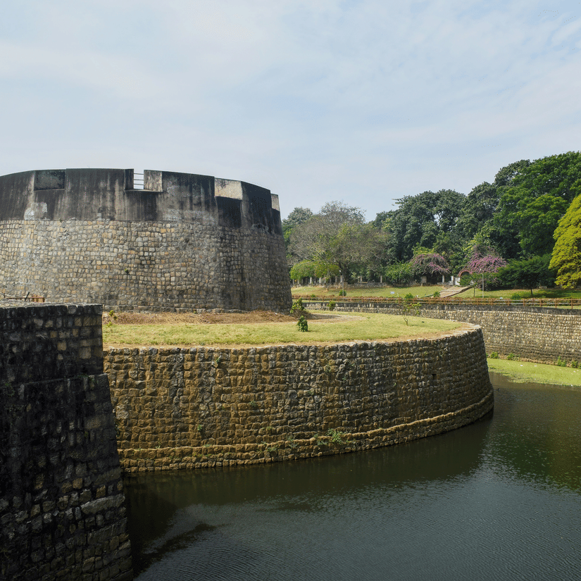 Palakkad Fort, one of the popular tourist places in Palakkad, beside calm water, surrounded by greenery under a bright sky, showcasing traditional architecture and peaceful surroundings