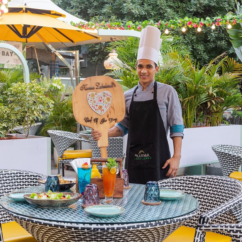 A chef holding a signage next to a table at Pizza Bay - Karma Lakelands.