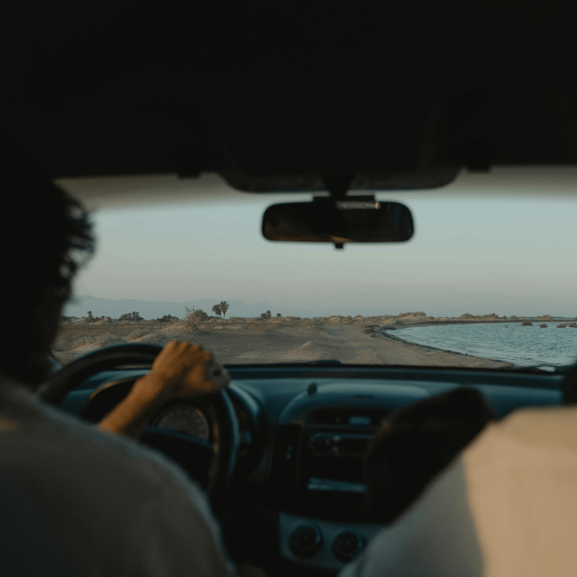 A scenic view from inside a car driving along the coast, with passengers enjoying the breeze and views of the blue sea.