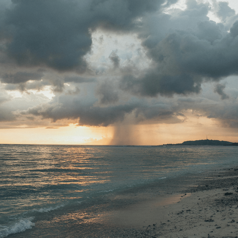 Rain falling over the ocean with the sun setting on the horizon, creating a moody scene.