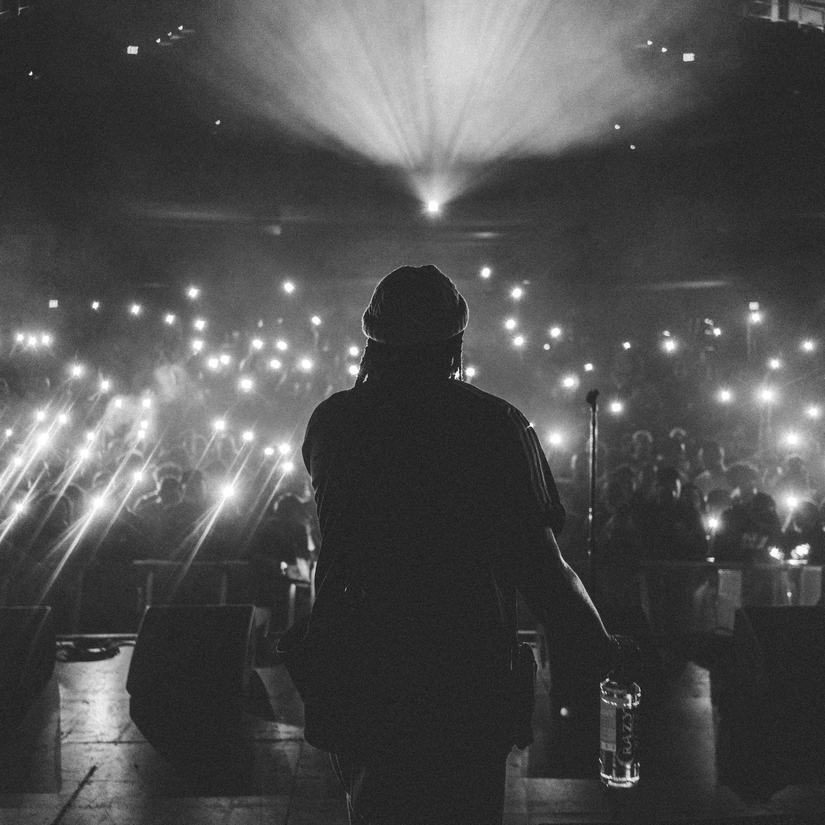 A view from the stage of a concert, where a performer is sitting in front of a large audience having their phone's flashlight on.