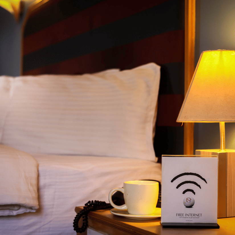 a bed with white linens with a wifi sign kept on the bedside table 2