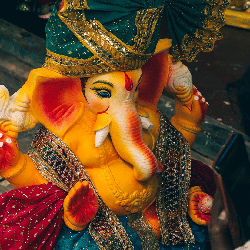 A brightly decorated idol of Lord Ganesha is featured wearing colorful traditional attire and a headpiece.