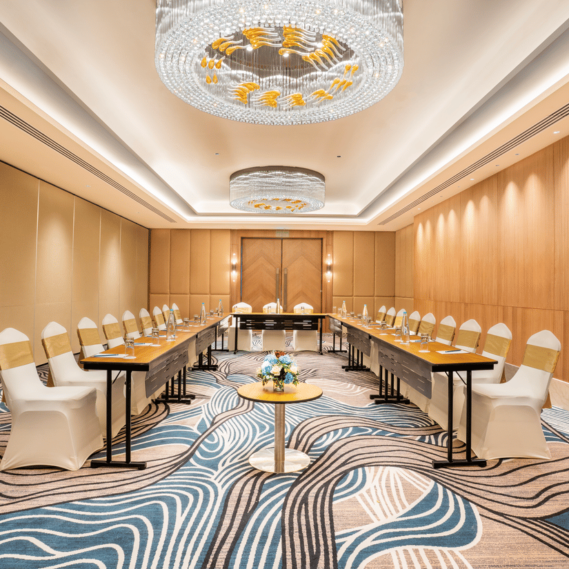 A conference room at Sarovar Premiere Alwar with round tables and chairs arranged on a patterned carpet floor.
