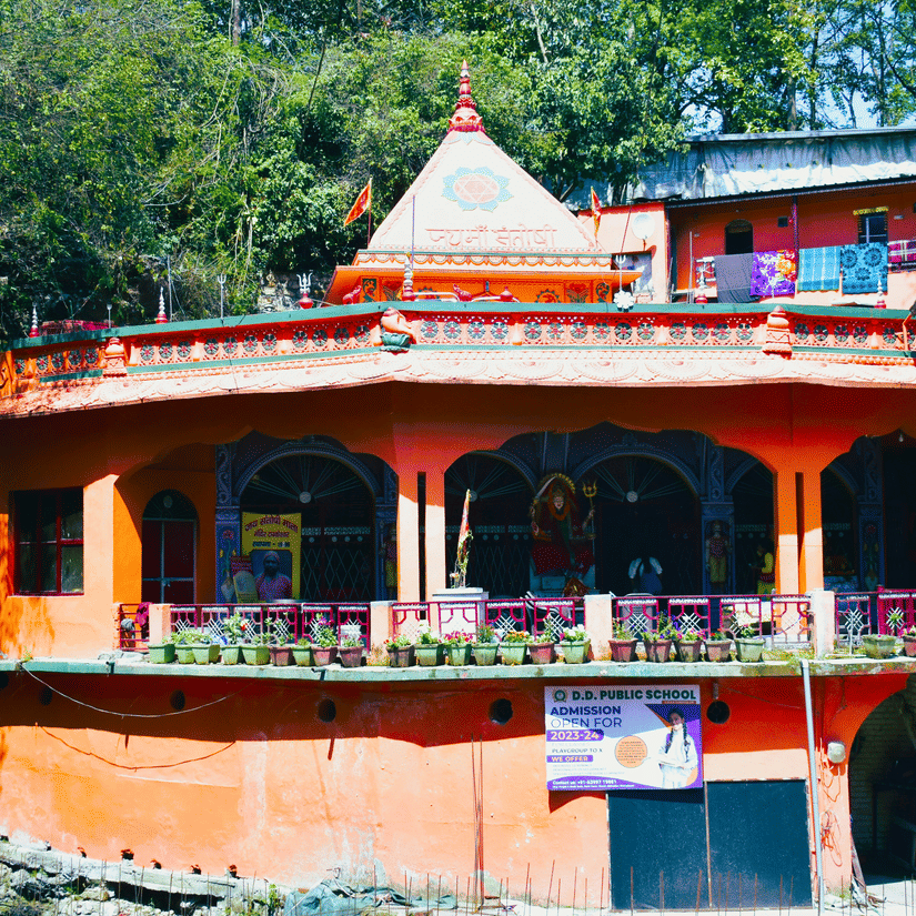 A view from distance of Tapkeshwar Temple, one of the popular Dehradun tourist attractions, with trees behind it and steps leading to the entrance.