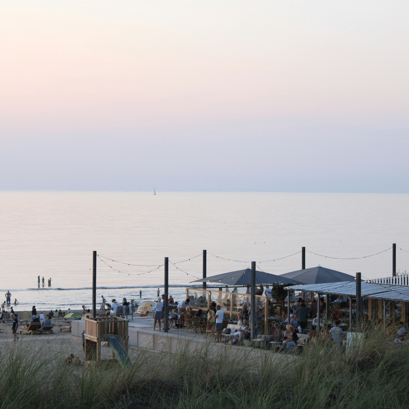 Beachfront open-air restaurant and bar with guests dining under string lights at dusk with calm ocean in the background