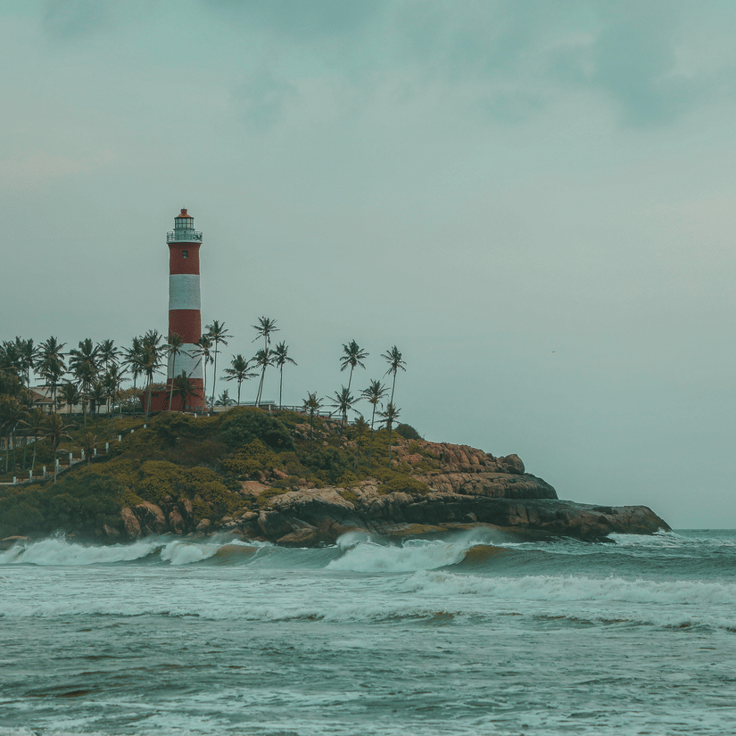 A lighthouse standing on a rocky coastline with waves hitting the shore under a cloudy sky.