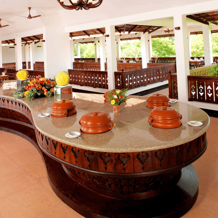 Ayurveda Restaurant near Kovalam Beach featuring a curved wooden buffet table with traditional clay pots and floral decorations at The Travancore Heritage Beach Resort.