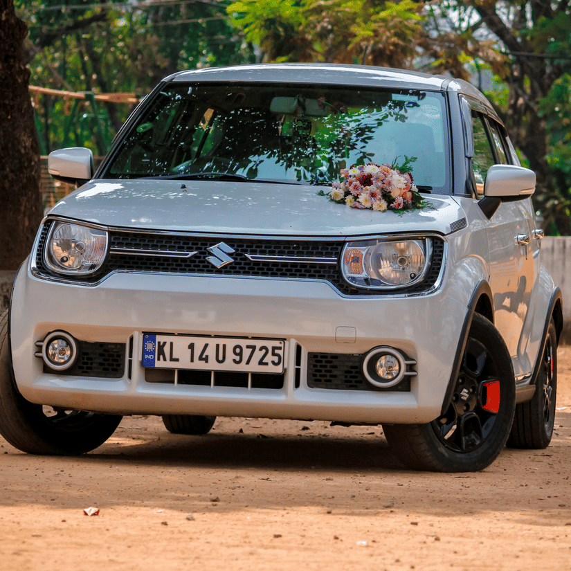 A Maruti Ignis parked on a muddy road with a bouquet on it's bonnet and trees in the background. Narmada Parikrama by car is one of the fastest ways to finish the pilgrimage.