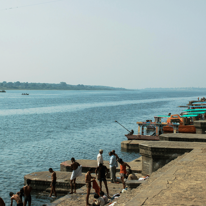 A view of Maheshwar Ghar near the banks of Narmada River with people taking a dip in the river, and boats parked along the end.