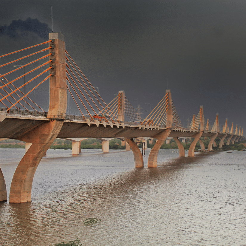 A view of the Narmada Cable Bridge, one of the best places to visit in Bharuch, over the Narmada River with a golden hue on it and dark clouds above.