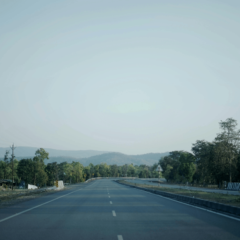 A wide, open highway stretching through a quiet rural landscape with trees on either side and distant hills under a clear sky.