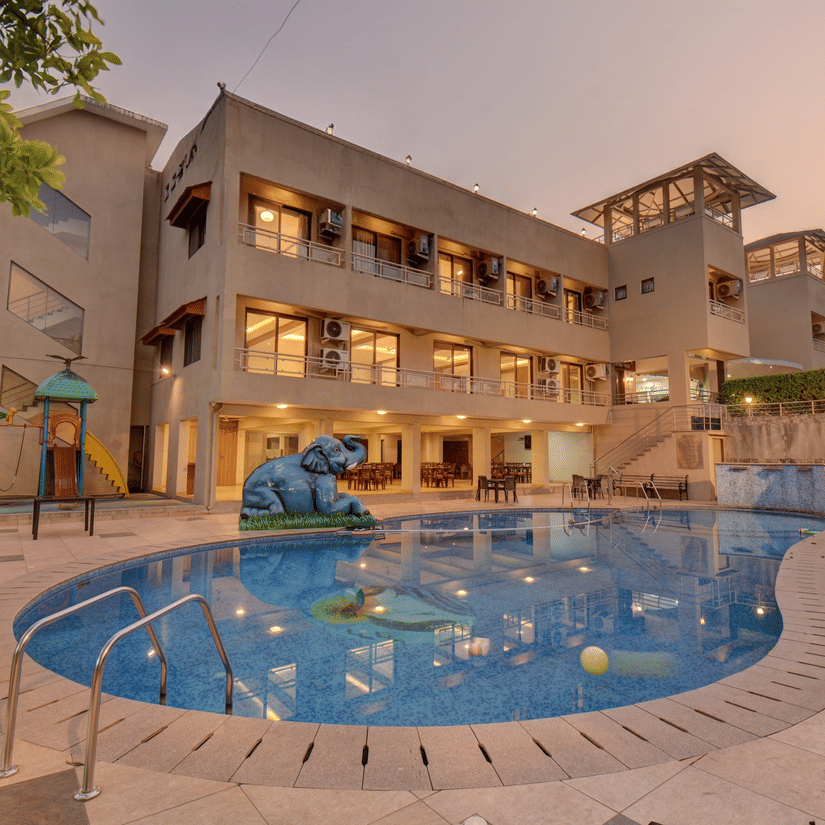 Evening view of the VITS Lonavala in the background and the pool in the foreground covered by trees on either side. This 4-star hotel is the best place for a destination wedding in Lonavala with it's lawn, which can accommodate 150 pax.