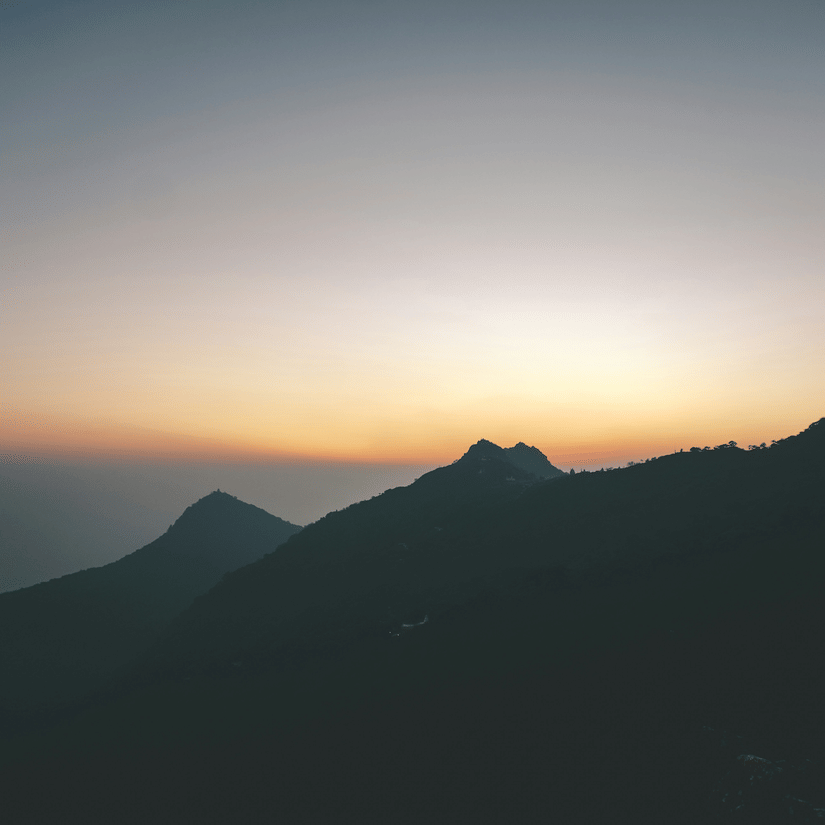 Early dawn view of layered mountain silhouettes at Parasnath Hill against a soft pastel sky before sunrise.