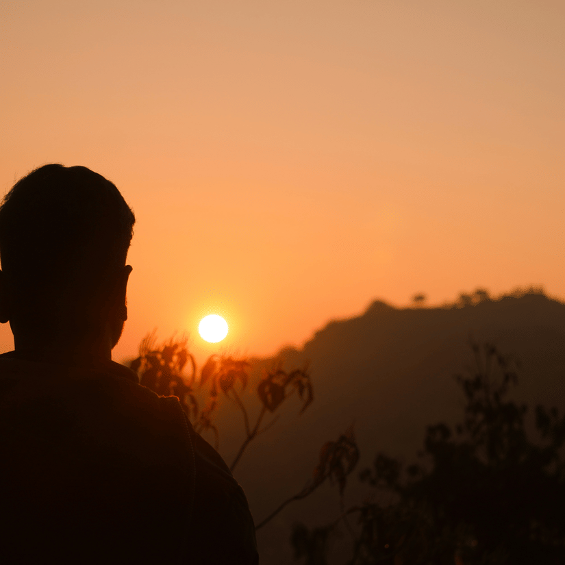 Silhouette of a traveller watching the sunrise over the mountains at Parasnath Hill with golden morning light across the horizon.