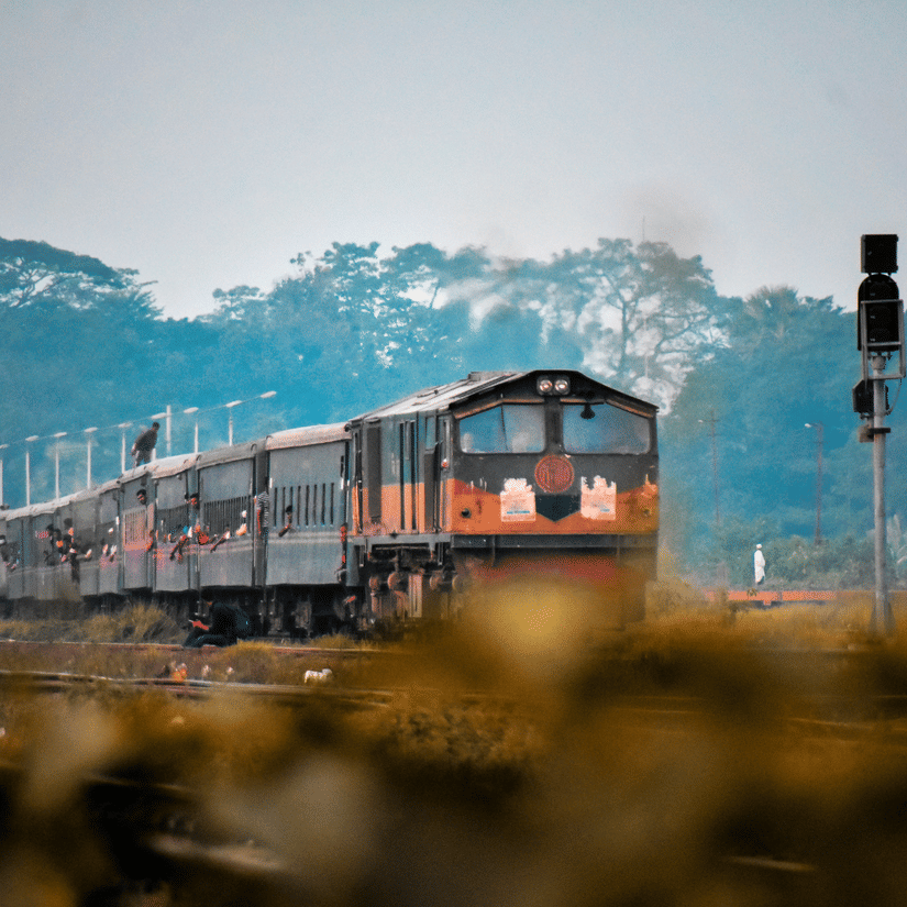 A train running on railway tracks with two signals and trees in the background
