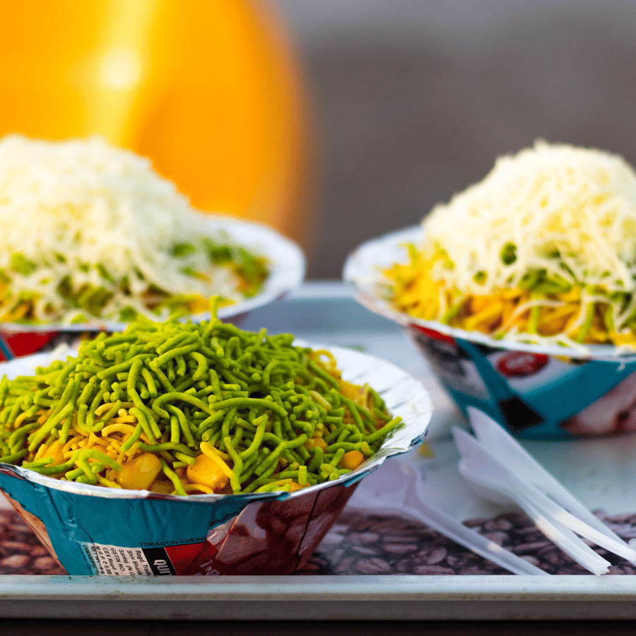 Three paper bowls of corn bhel, a famous Indian street food.