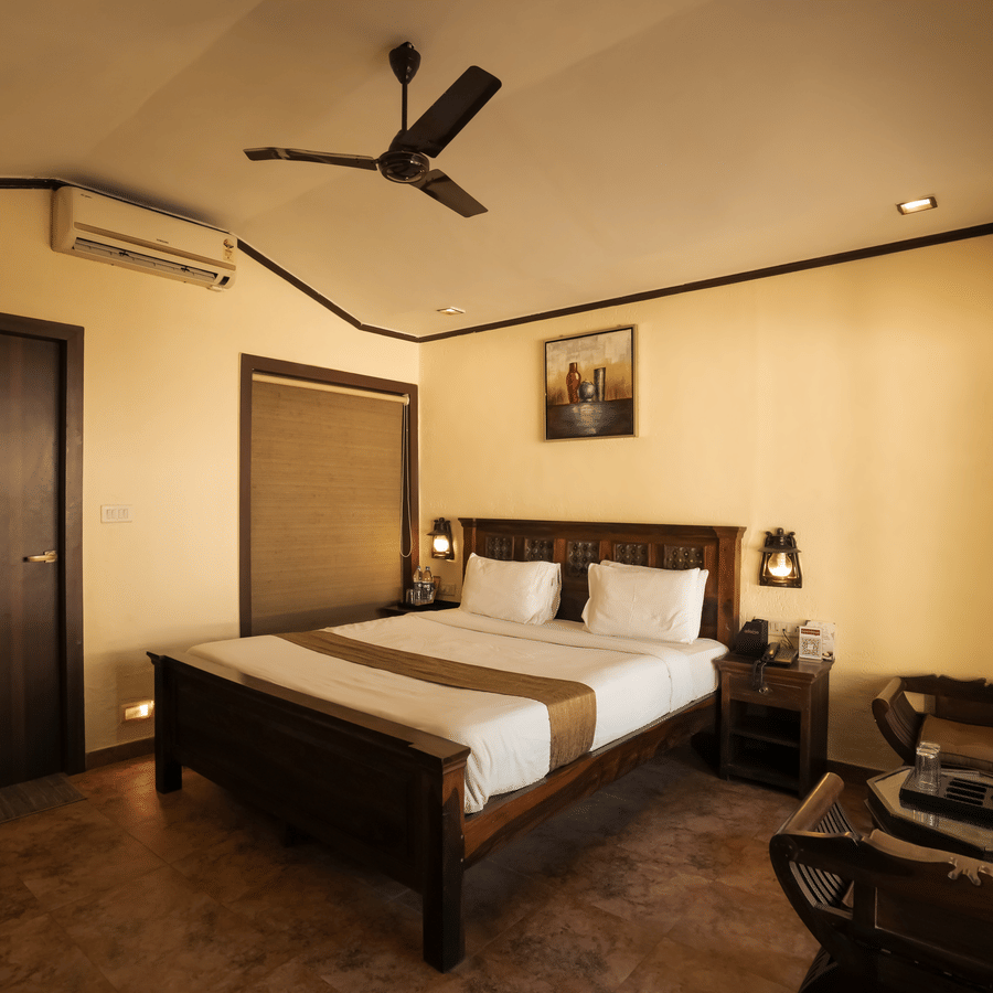 A warm-toned resort bedroom featuring a dark wood double bed frame, bedside lamps, and a coffee corner setup.
