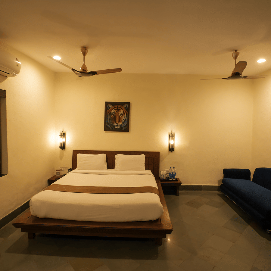 Hotel room showing a neatly made double bed flanked by a blue sofa and dark tiled flooring.