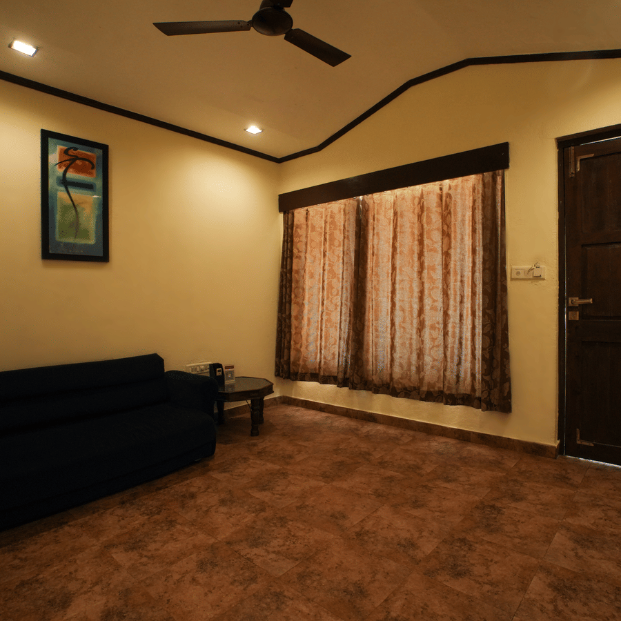 A hotel room seating area with a dark blue sofa, patterned carpet, a wooden door, and draped windows.