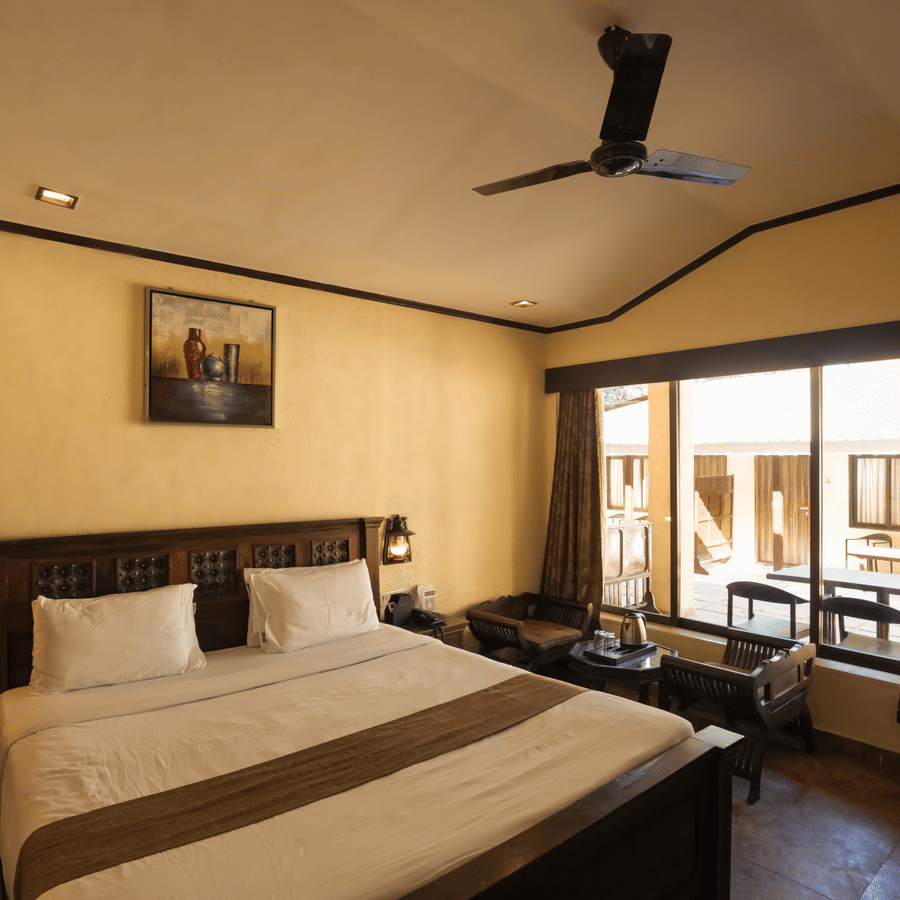 A cozy resort bedroom featuring a double bed, wooden furniture, and a large window overlooking the outdoor property.