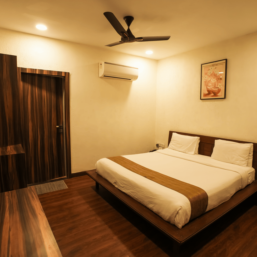 A well-lit hotel bedroom featuring a neat double bed with white linens and dark wood accents.
