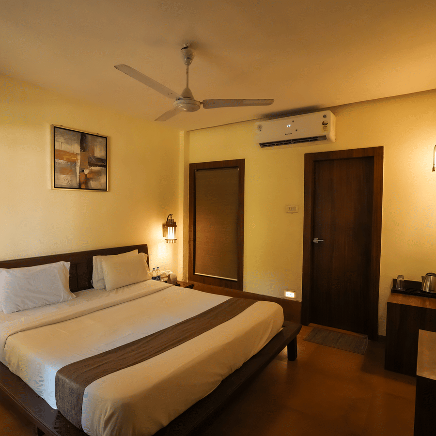 Hotel bedroom with a double bed, wall-mounted television, wooden door, and ambient wall-sconce lighting.