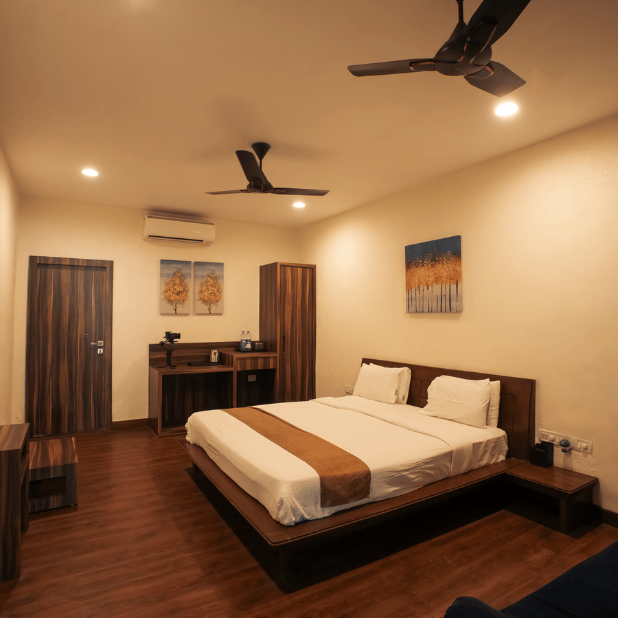 A well-lit resort bedroom featuring a double bed, dark wooden flooring, dual ceiling fans, and minimalist furniture.