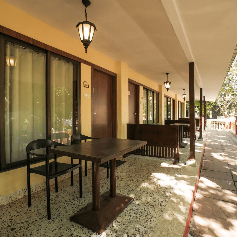 A shaded outdoor patio area outside a resort room featuring a small table and black chairs on a paved walkway.