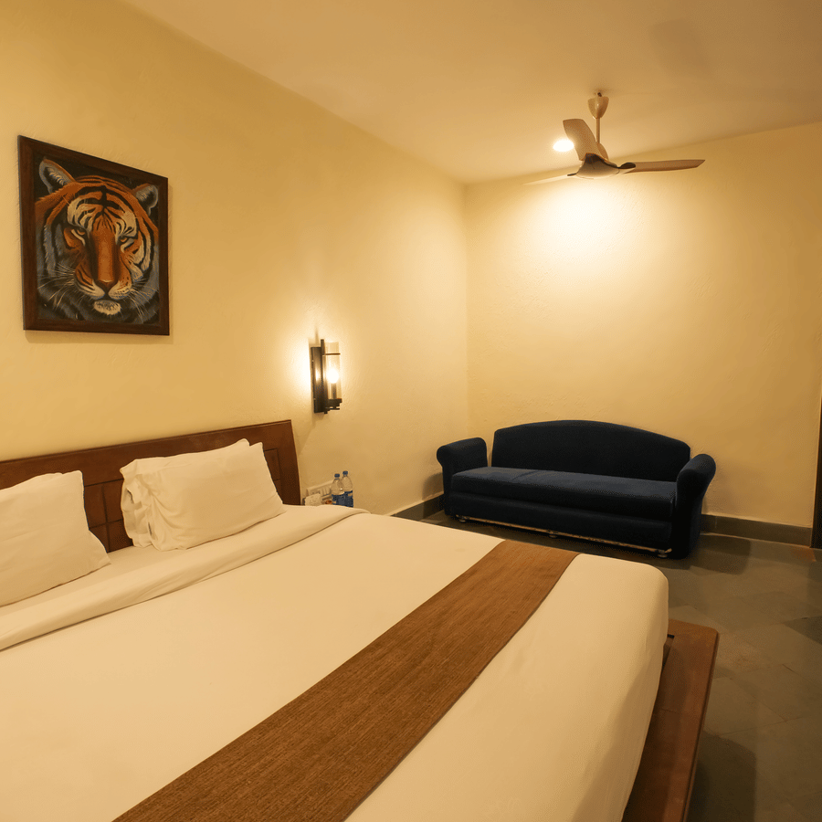 A spacious hotel room featuring a large bed, a small blue couch in the corner, and a framed art piece.