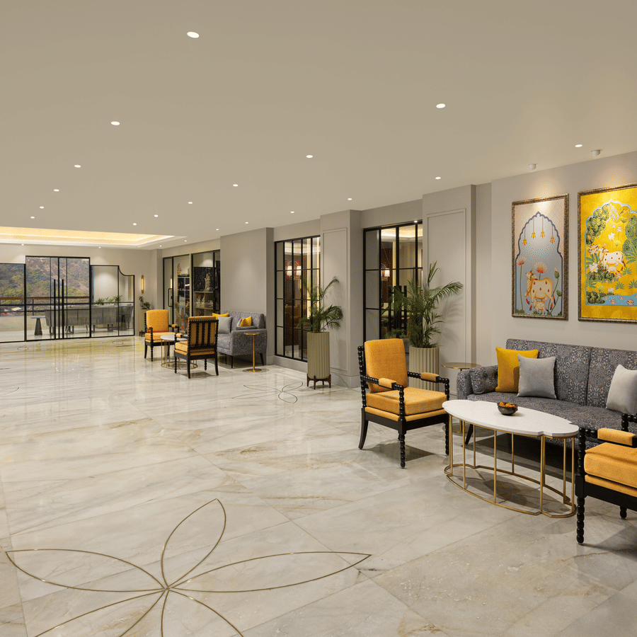 Spacious hotel atrium with marble floors, yellow-accent seating, framed artwork, and warm recessed ceiling lighting creating a modern lounge ambience.