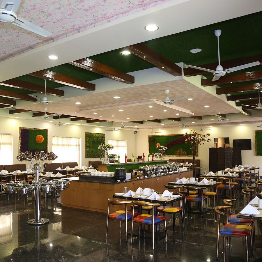 In-house restaurant of GK Hill View Resort with parallel aligned tables, overhead lighting.