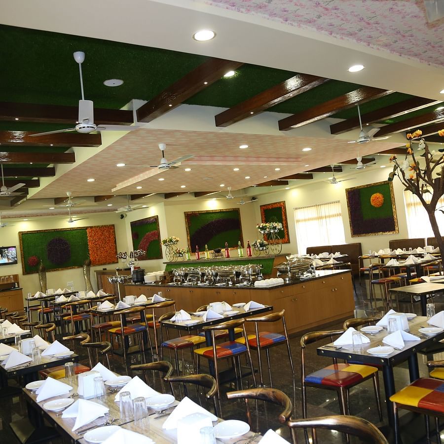 In-house restaurant of GK Hill View Resort with parallel aligned tables, overhead lighting.