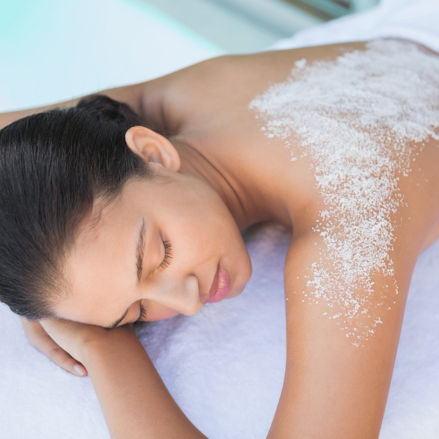 Woman enjoying a spa treatment with a white exfoliating scrub spread on her back.