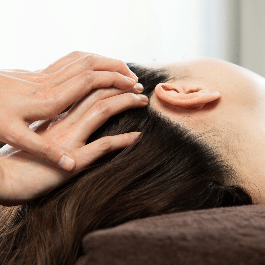 Woman lying on a spa table, receiving a head massage.