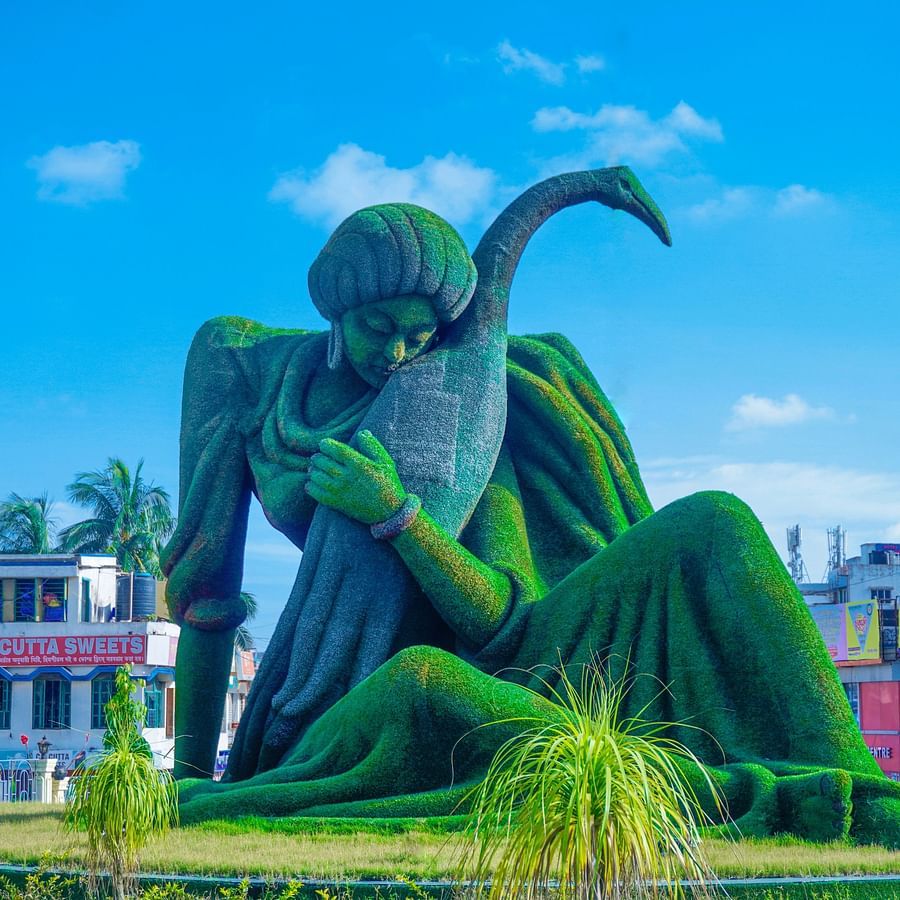 A statue covered in green cloth of a woman hugging a bird