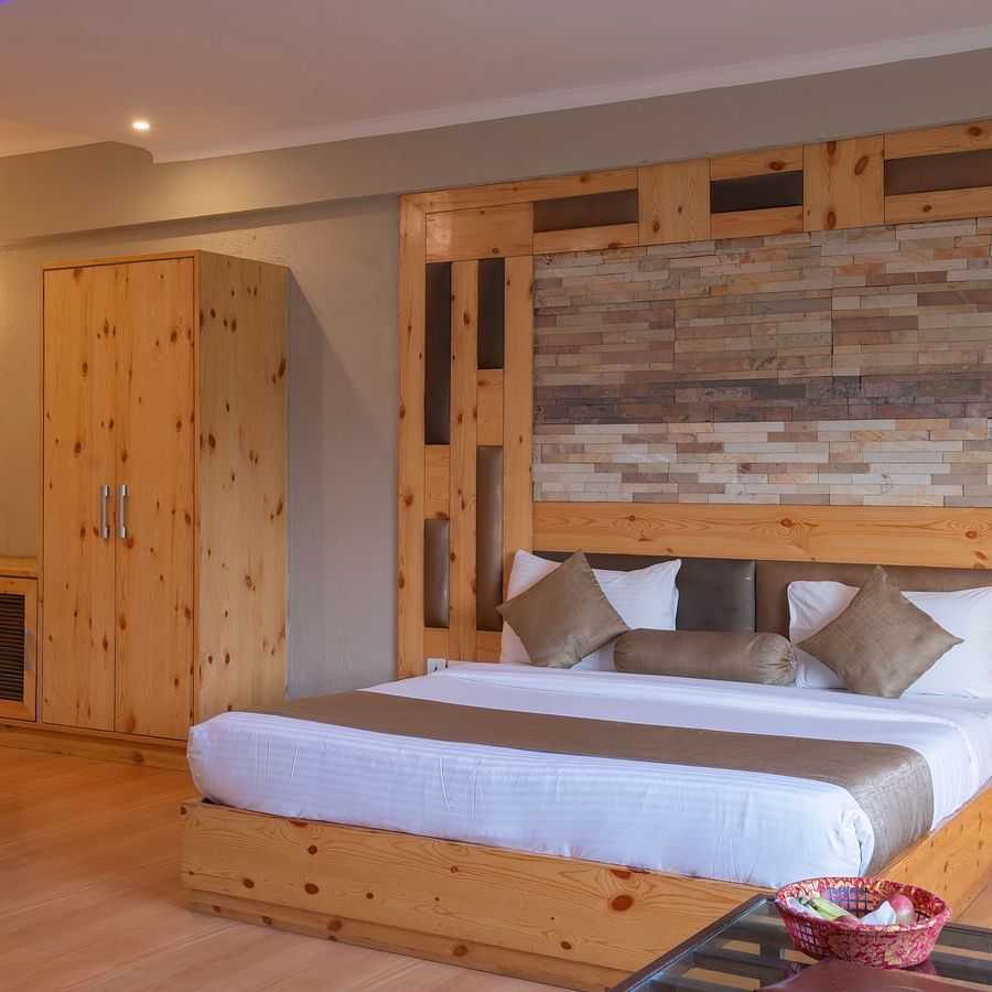 A comfortable king bed with wooden floor and wardrobe at The Tattwaa Corbett Spa & Resort.