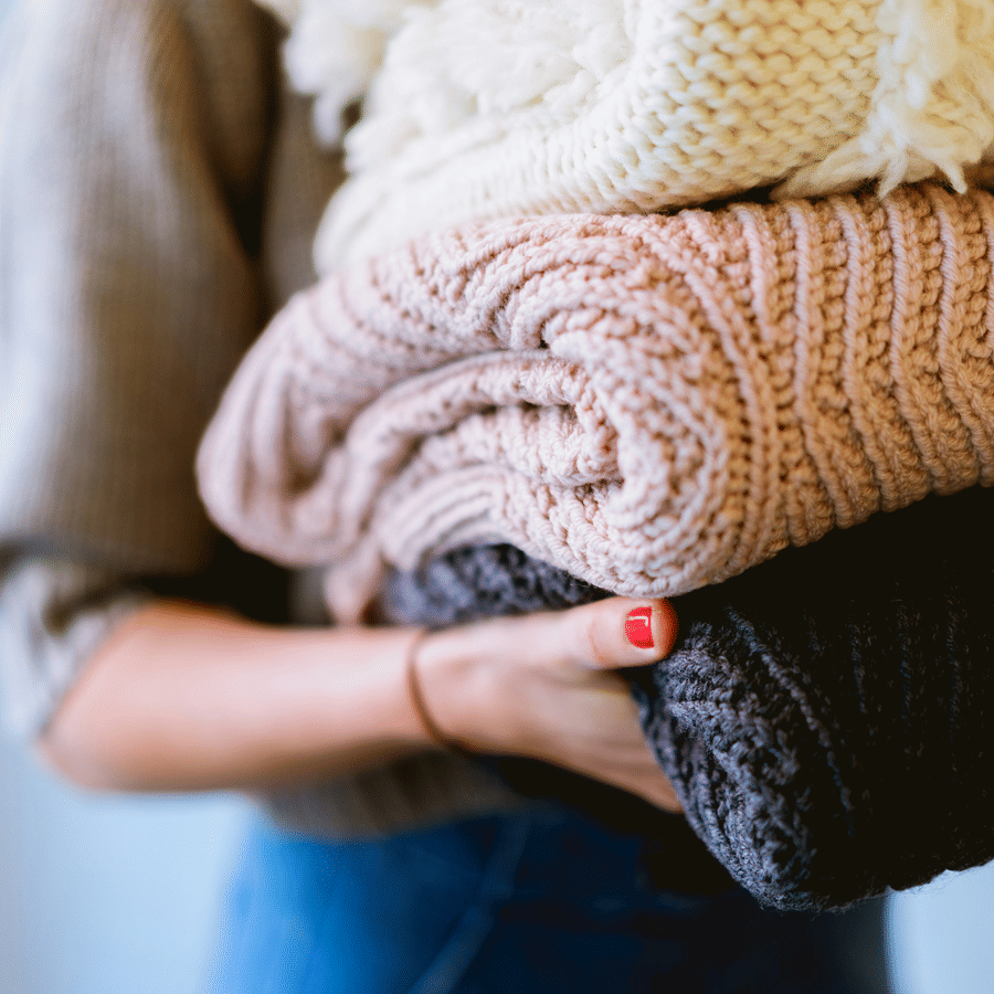Person holds a stack of folded knitted blankets in hand, shown from the side, V FIVE HOTEL.