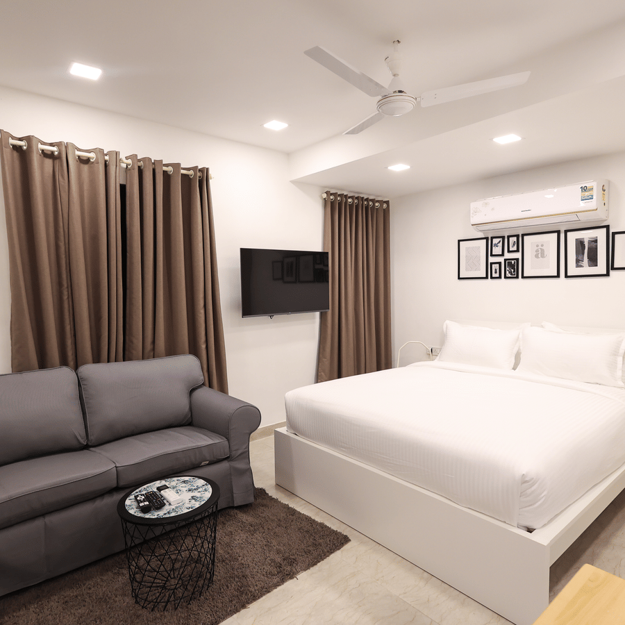 A spacious room featuring a large bed, a 2-seater sofa, a wall-mounted TV, and an A/C unit at Wabi - Sabi by Alamiko, Juhu. 