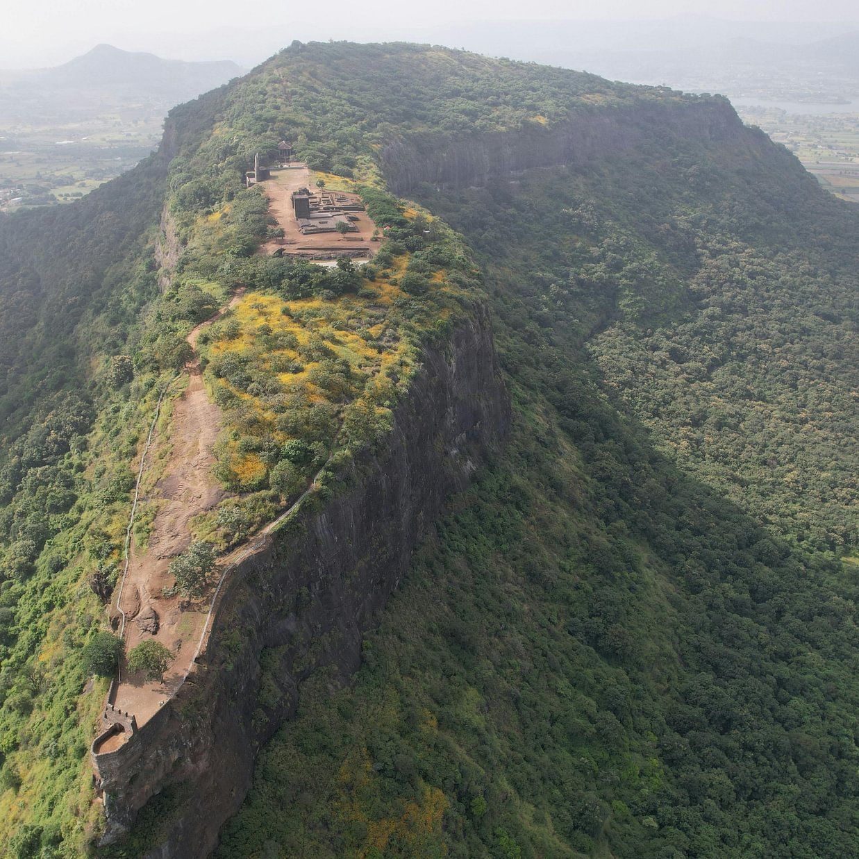 Aerial view of a historic hilltop fort surrounded by dense greenery and steep cliffs.