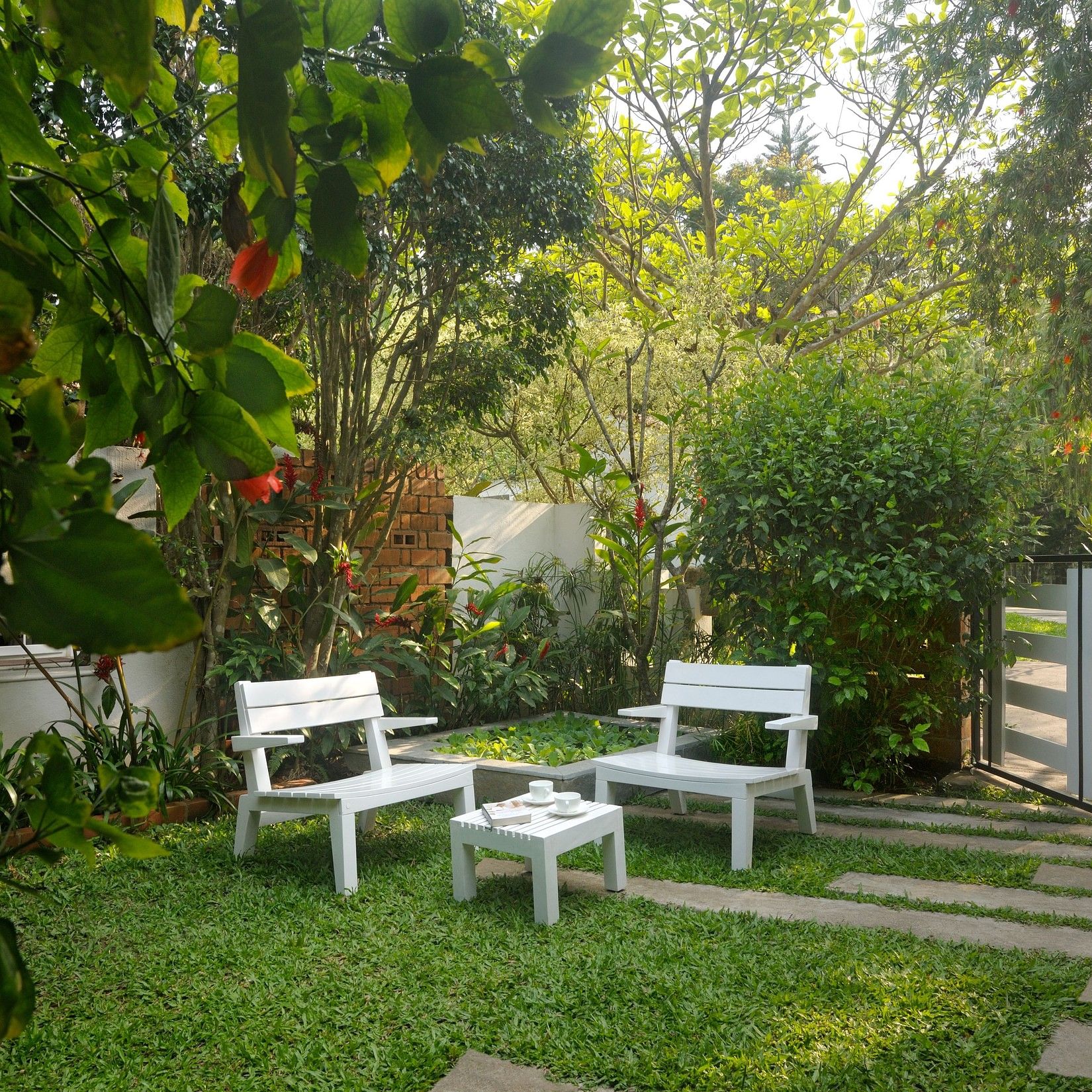 White outdoor seating arrangement in a garden with lush plants and a walking path at Amanvana Spa Resort, Coorg - Luxury Resort