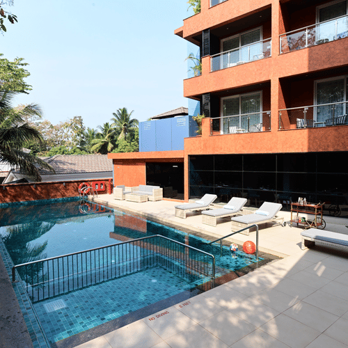 The outdoor swimming pool area with lounging chairs placed besides it at Golden Tulip Vagator, Goa