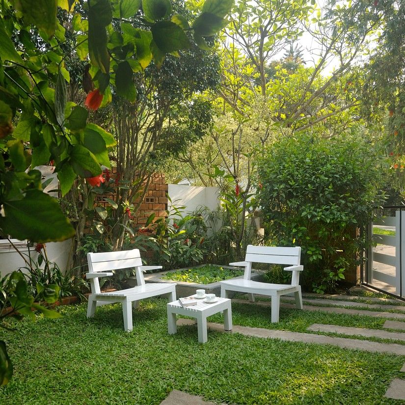 White outdoor seating arrangement in a garden with lush plants and a walking path at Amanvana Spa Resort, Coorg - Luxury Resort