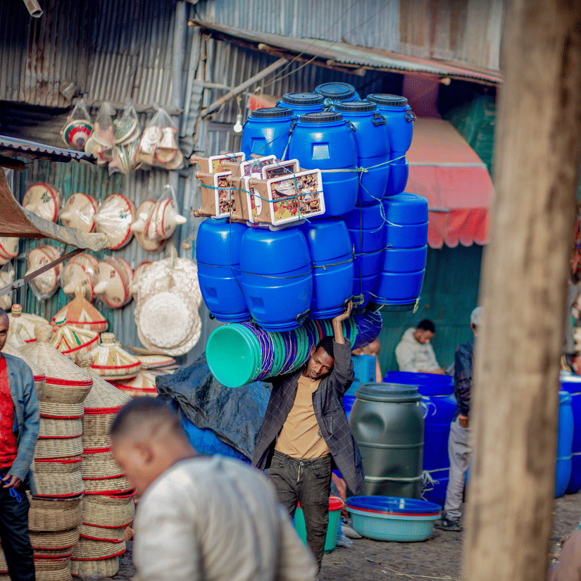 An overview of a person carrying numerous plastic barrels for water storage in Mercato Market.