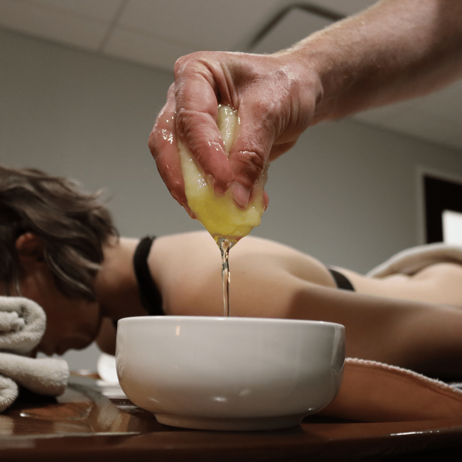 A person lying on their stomach as a hand is squeezing the liquid out of  the sponge into a bowl at YO1 Longevity & Health Resorts, Catskills