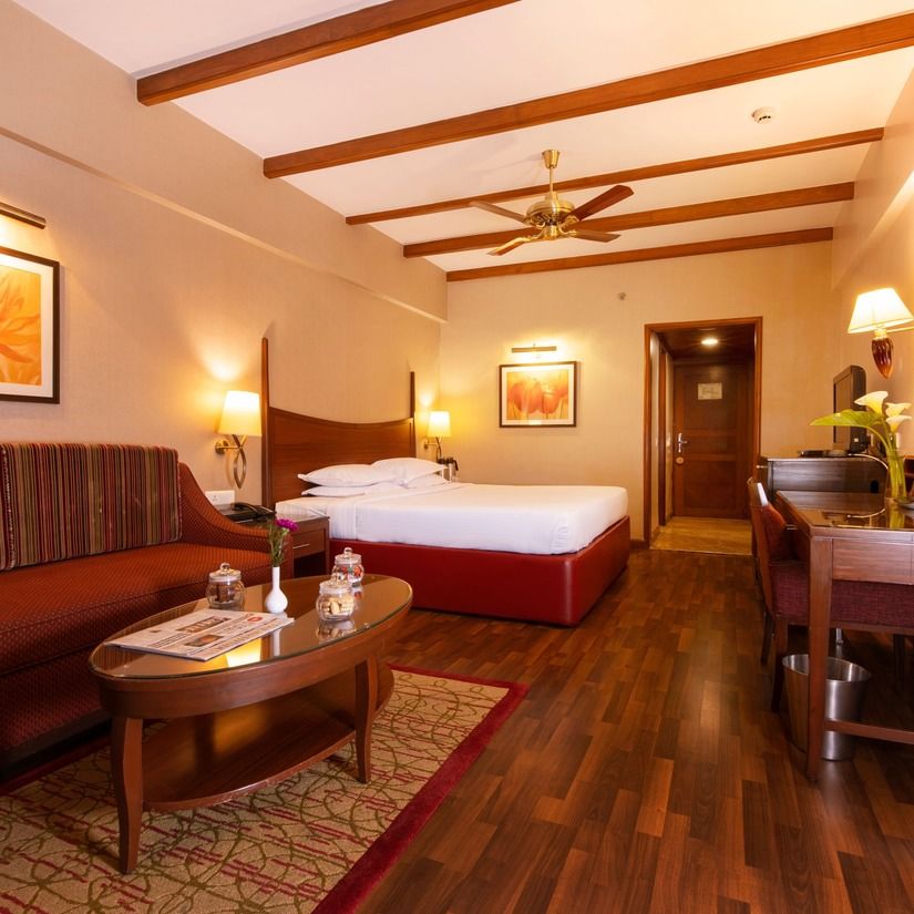 An image of a bedroom featuring a double size bed, a work desk and chair, TV screen, a sofa and centre table - The Carlton