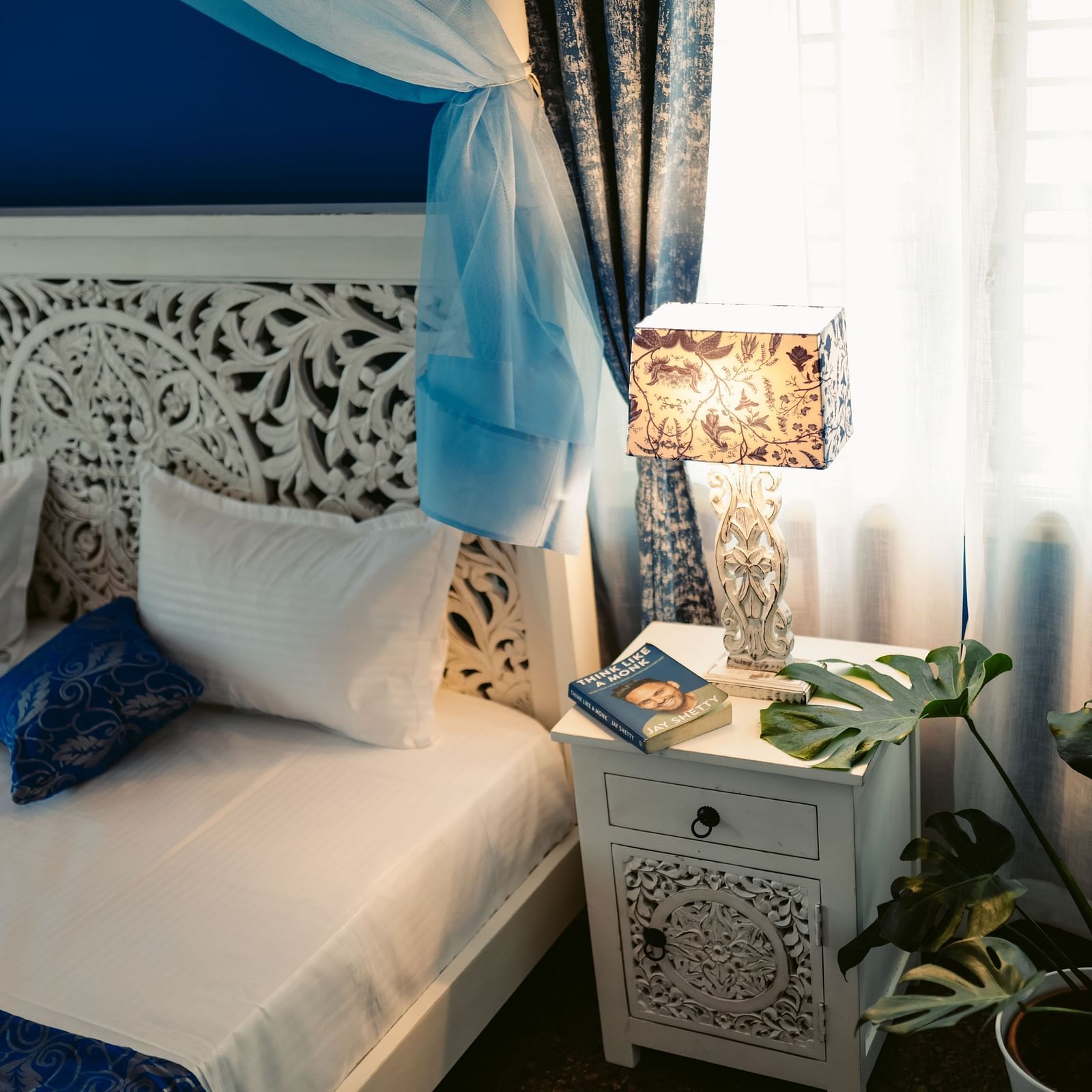 A close-up of a white ornate headboard with pillows, a side table with a lamp | Adhyaya Heritage Reverbed