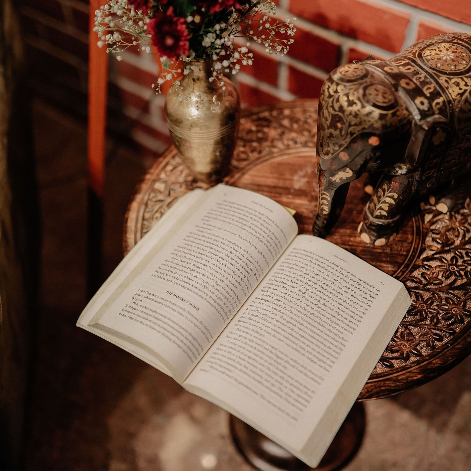 Open book on a small table with decorative items, with a glimpse of a green armchair  | Adhyaya Heritage Reverbed